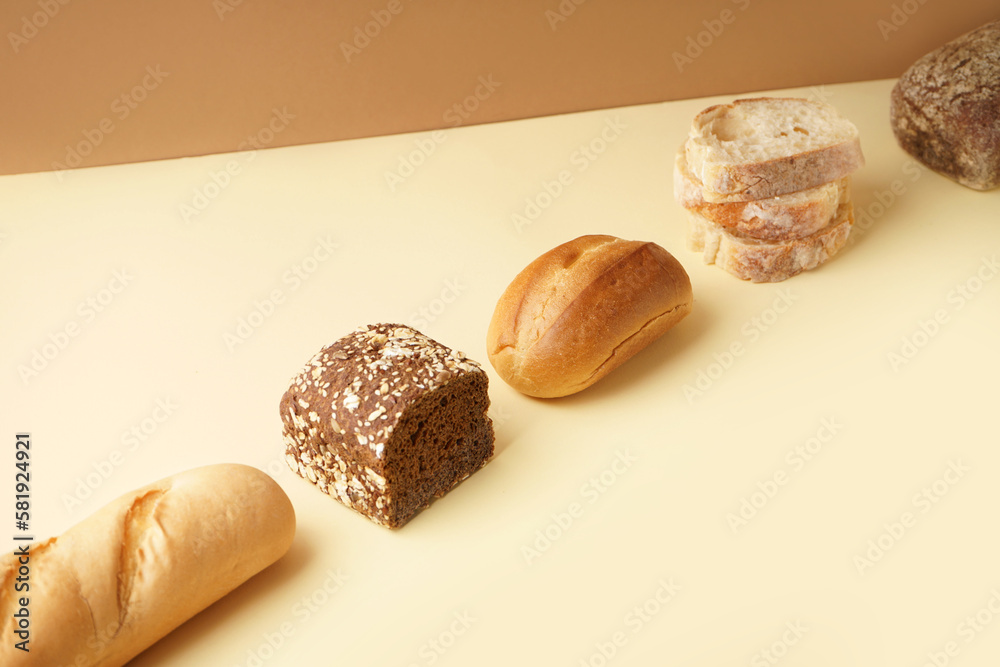 Loaves of different bread on beige table near brown wall