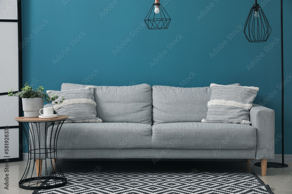 Grey sofa with cushions and houseplant on table near blue wall