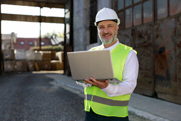 portrait of the man builder in helmet and vest using wireless laptop for improving blueprints while 