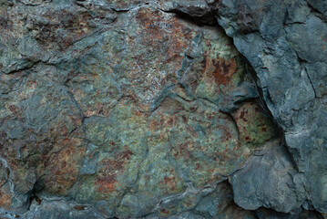 Textured rock fragment of different rocks with cracks and lichen.