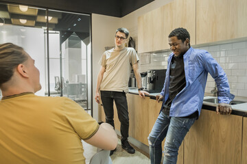 Group of cheerful young people talking and smiling during coffee break time in the office. Team of professional software developer relaxing in the canteen.