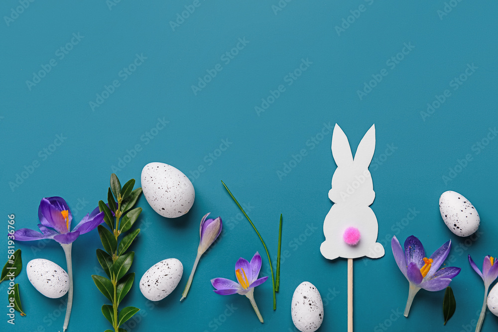 Composition with Easter eggs, paper bunny, beautiful crocus flowers and plant leaves on blue background