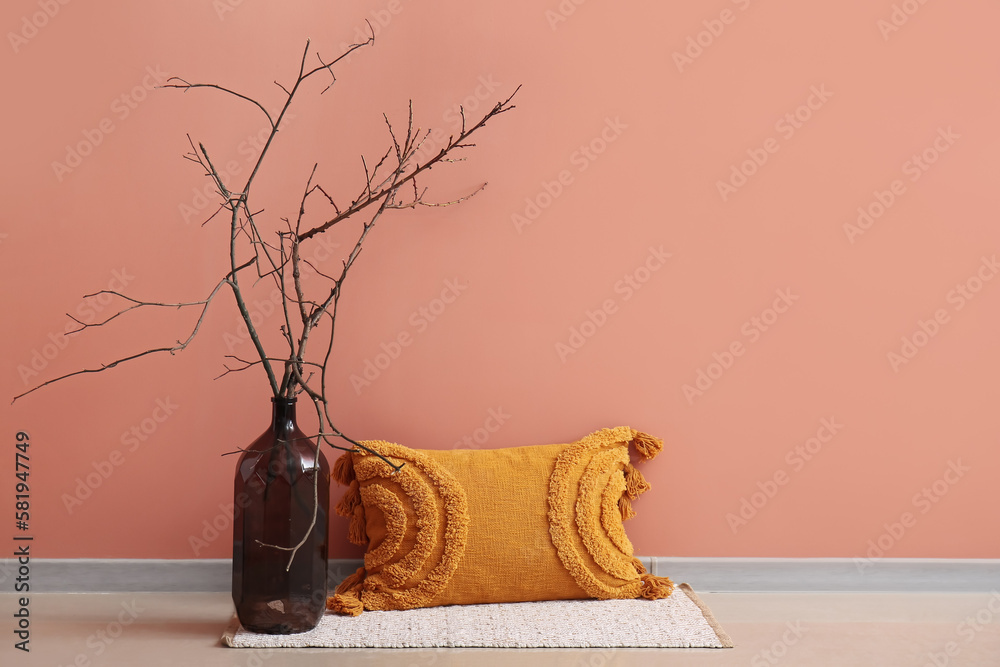 Stylish decorative pillow and bottle with ikebana near pink wall