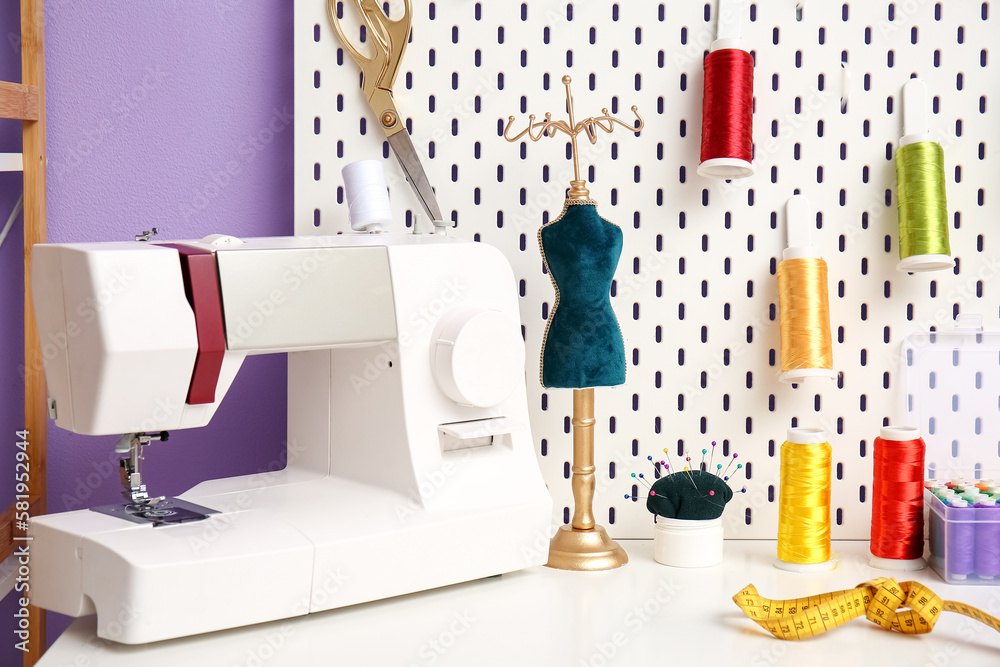 Sewing machine, mannequin and pegboard with thread spools on table in atelier, closeup