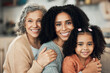 © Allistair/peopleimages.com - Happy family, portrait and hug by girl with mother and grandmother on sofa, smile and sweet on blurred background. Face, row and generations of women relax on couch, bond and embrace in living room