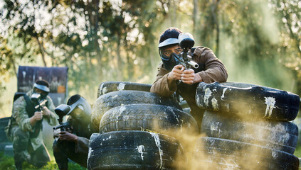 Canvas Print - Team, paintball and tires for cover bunker or protection while firing or aiming down sights together in nature. Group of people waiting in teamwork for opportunity to attack or shoot in extreme sport