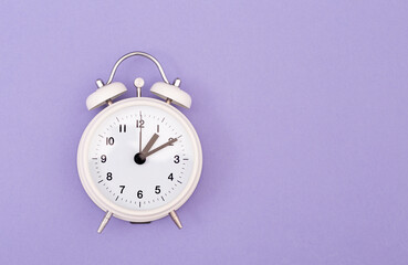 Reloj despertador color blanco ilustrando cambio de horario primavera, verano sobre fondo morado