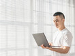 © Anciens - Asian man is using laptop near the window.
