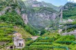 Terraced lemon groves and picturesque houses in a scenic valley behind the coastal Italian town of Amalfi in Salerno province, with smoke drifting across the steep background hills.