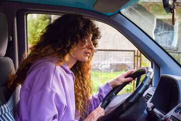 Independent curly hair backpacker woman driving scared lost during an adventure road trip with her camper van