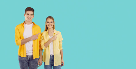 Happy couple showing something on turquoise blue copy space background. Young man and woman in casual clothes pointing to empty copyspace side and smiling. Advertising concept