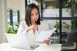 © bongkarn - Concentrated Asian businesswoman reviewing or examining business reports at her desk.