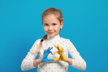 Wall Mural - Little girl making heart with her hands painted in Ukrainian flag colors on light blue background. Love Ukraine concept