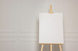© New Africa - Wooden easel with blank canvas near white wall. Space for text
