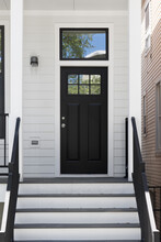 Front Door And Porch Of A White Modern Farmhouse With A Black Front Door And Railings.