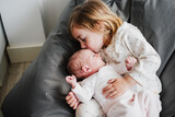 Fototapeta Łazienka - happy big sister toddler kissing newborn baby girl at home during daytime.Family and childhood