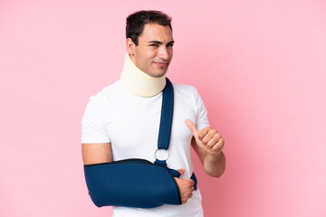 Wall Mural - Young caucasian man with broken arm and wearing a sling isolated on pink background proud and self-satisfied