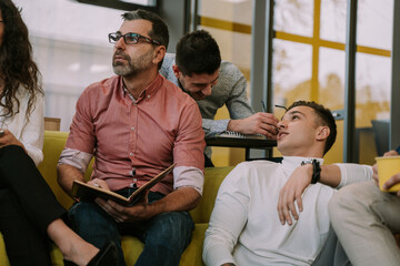 Two young people having fun conversation while their colleagues are brainstorming