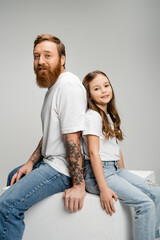 Wall Mural - Smiling father and daughter sitting back to back on cube isolated on grey.