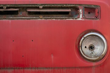 Sticker - Closeup shot of the front part of an old vintage rusty red car on the blurred background