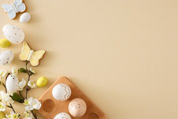 Wall Mural - Easter celebration idea. Flat lay photo of colorful easter eggs in wooden holder butterfly cookies and cherry blossom branch on isolated beige background with copyspace