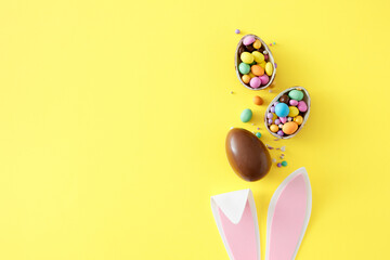 Wall Mural - Easter sweets concept. Top view photo of rabbit bunny ears chocolate eggs with сolorful candies on isolated yellow background with empty space