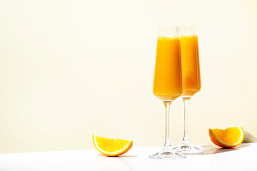 Wall Mural - Mimosa alcohol cocktail drink with orange juice and cold dry champagne or sparkling wine in glasses. Beige background, hard light, shadow pattern