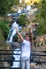 Rear view happy young woman arms raised at waterfall background. Lady looking back looks at camera enjoying at tropical nature waterfalls banner panoramic. Travel vacation concept. Copy ad text space