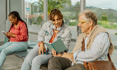 Multiracial people reading a book while waiting at tram station in the city