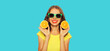Summer portrait of happy smiling young woman with slices of fresh orange fruits wearing sunglasses on blue background