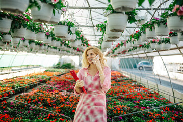 Wall Mural - Young woman working in a greenhouse and using a smartphone