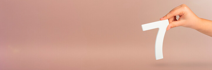 Fototapete - Number seven in hand. Hand holding white number 7 on red background with copy space. Concept with number seven. Birthday 7 years, percent, seventh grade or day.