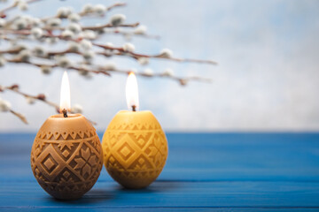 Traditional Easter decor. Burning soy candles in the shape of colorful eggs and willow twigs on a blue textured background. Happy easter.Colorful easter candles and flowers on background.