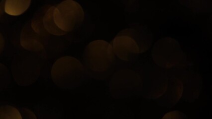 Wall Mural - Smooth Motion Of Gold Sepia Bokeh On Black Background. Horizontal appear and disappear of defocused lights circles. Abstract moving background of glow simmering bokeh in sepia tones.