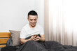 © Anciens - Asian man is using mobile phone in the bed.