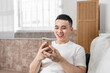 © Anciens - Asian man is using mobile phone sitting on the couch.