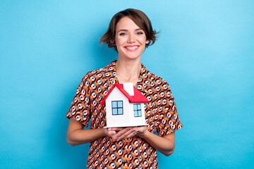 Sticker - Photo of pretty cheerful woman wear print blouse smiling holding small red roof house isolated blue color background