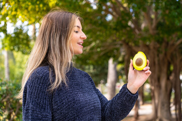 Wall Mural - Young pretty Romanian woman holding an avocado at outdoors with happy expression