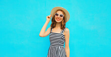 Summer portrait of beautiful young woman wearing straw round hat, striped dress on blue background