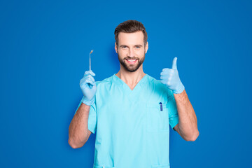 Sticker - Portrait of joyful cheerful dental assistant in lab blue uniform gesturing thumbup approve advice yes done sign with finger, having tool in hand, isolated on grey background