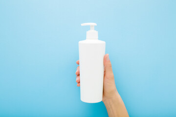 Wall Mural - Young woman hand holding and showing white big plastic pump bottle on light blue table background. Pastel color. Care about clean and soft body skin. Daily beauty product. Closeup. Top down view.