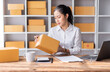 © David - Portrait of Starting Asian female small businesses owners SME entrepreneur working at Laptop in home Warehouse, online marketing, packing boxes, SME sellers, concept, e-commerce team, online sales.