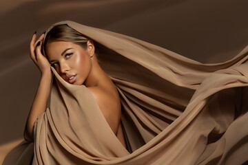 Beautiful Girl Face with Natural Makeup and Sun Tanned Skin. Beauty Woman wrapped in Brown Silk Fabric waving on Wind. Fashion Model Portrait wearing Head Satin Scarf