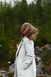 © Laura Chouette/Wirestock Creators - Vertical shot of a young Caucasian female walking in a forest wearing a white coat