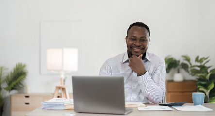 Wall Mural - Professional male economist searches needed information on portable computer, happy to recieve high net profit, spends important banking operation. Black male trader analyzes financial market