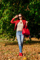 Poster - Young woman in fashion red jacket and blue jeans in autumn park