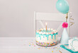Birthday party table with vanilla cake, balloon, hat, and candle on a light grey white background
