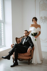 Wall Mural - groom in a black suit tie and the bride in a bright studio