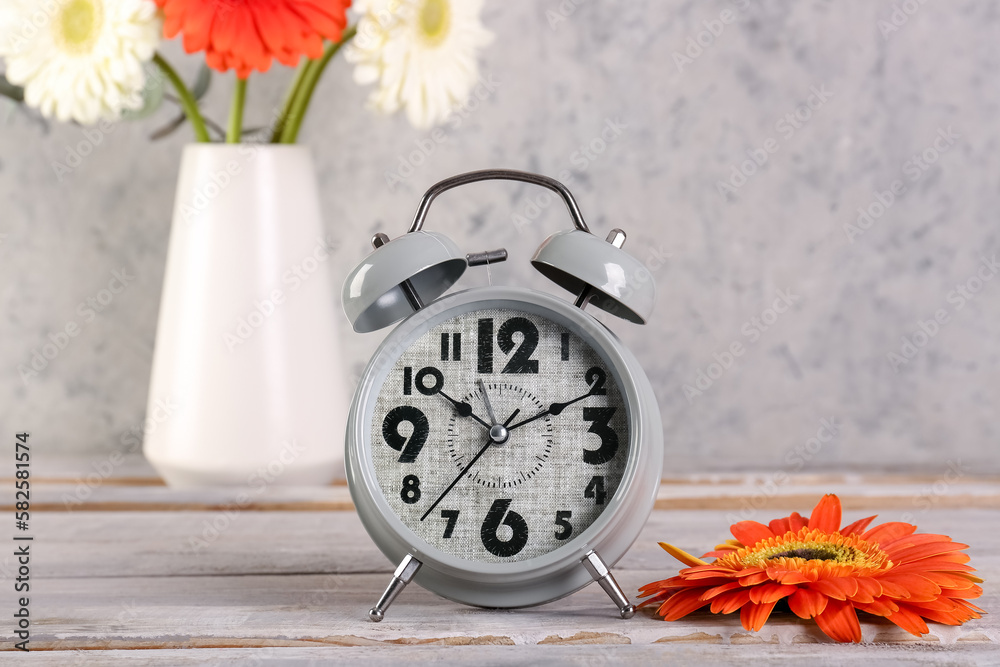 Alarm clock and beautiful gerbera flower on grey grunge background