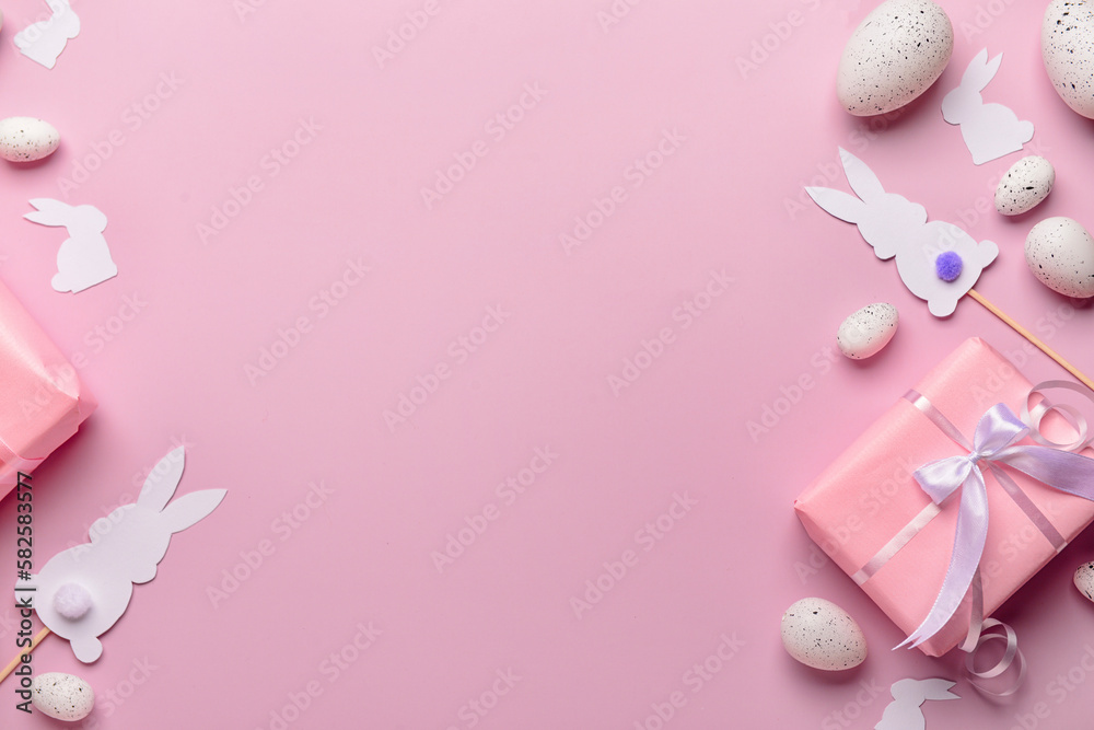 Frame made of Easter eggs, gifts and paper rabbits on pink background